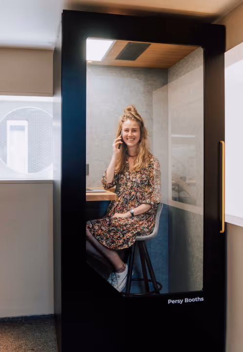 Woman sitting inside a black Persy Booth making a private phone call.