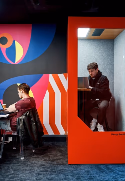 Employee working inside a red Persy soundproof booth in a colorful office