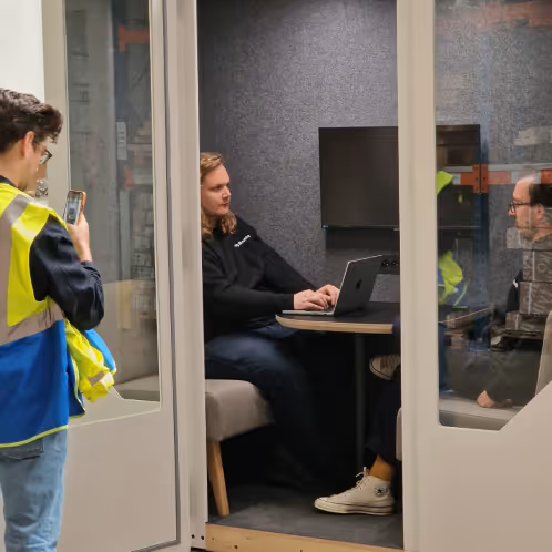 Two colleagues having a conversation inside a gray Persy office pod