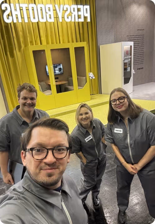 Persy Booths team standing in front of a bright yellow soundproof office pod