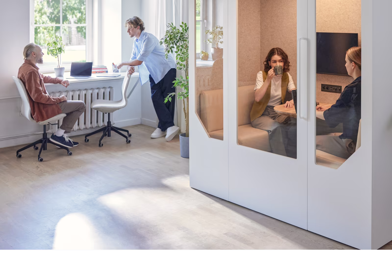 Employees collaborating near a phone booth in a modern office environment