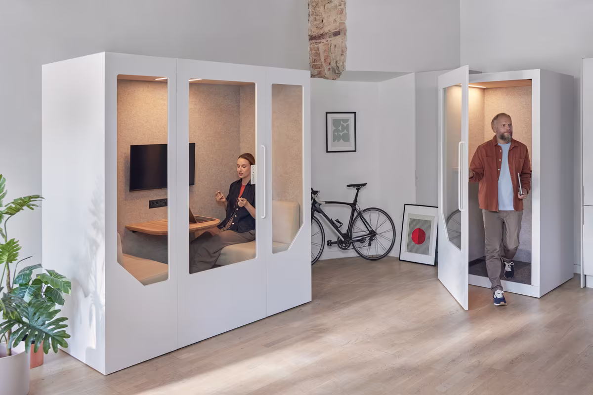 Employee entering a meeting pod while others use acoustic booths in the office