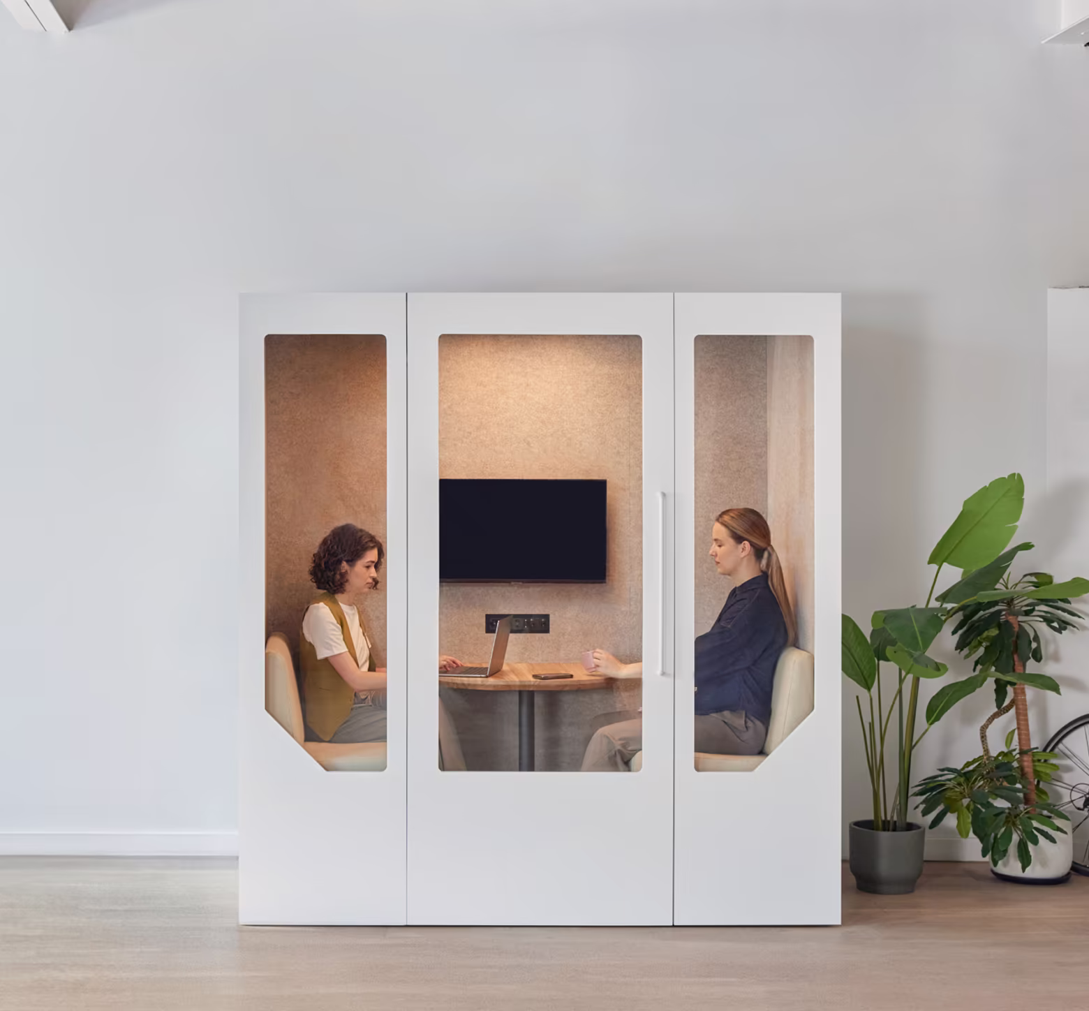Two colleagues having a private meeting inside a Persy soundproof booth in an open office