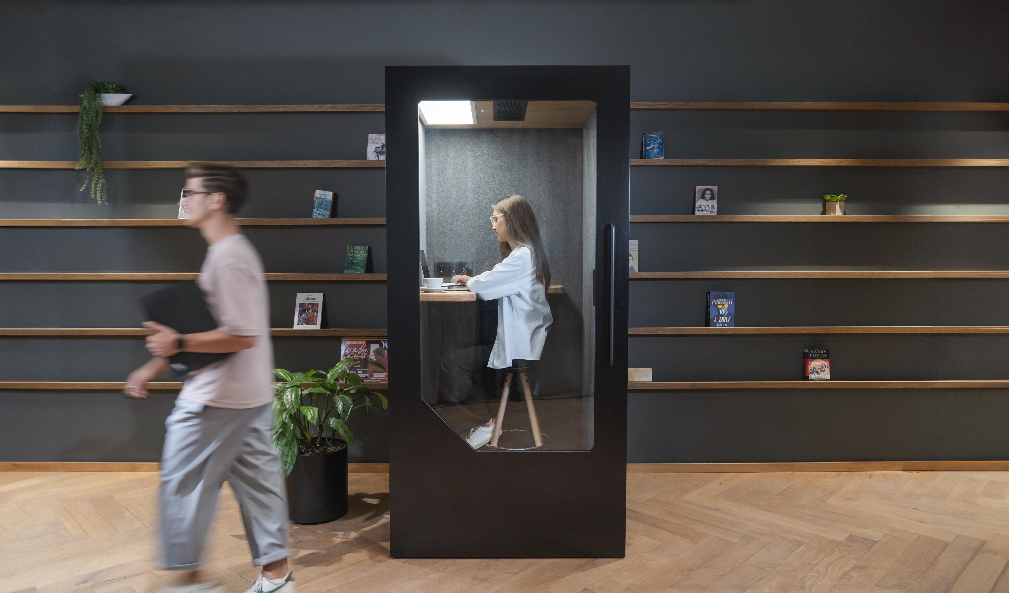 Person working focused inside a Persy Booths phone booth in a modern office library