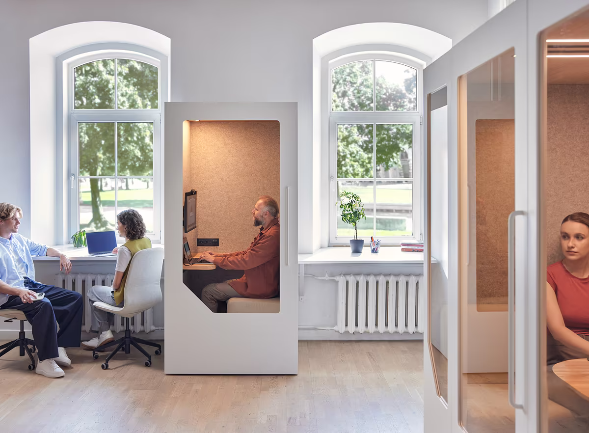 Team members working productively in an office environment with a Persy soundproof booth visible in the background