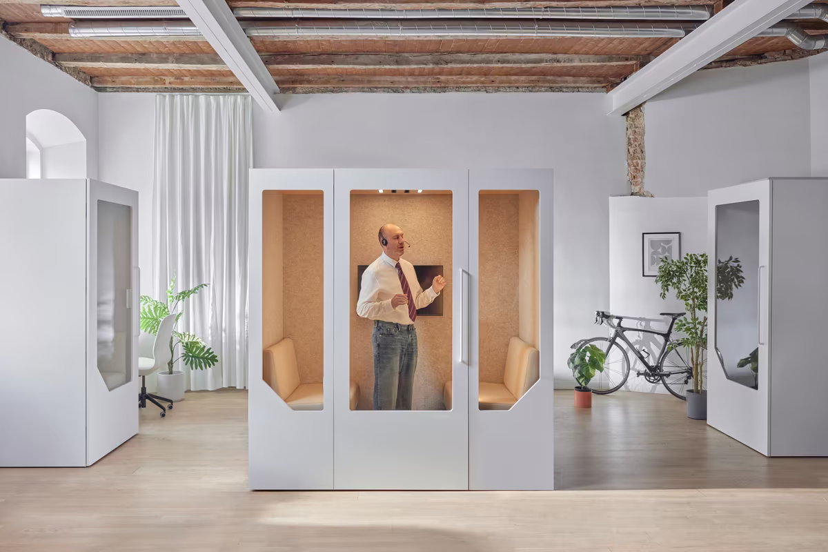 Employee taking a call inside a soundproof office phone booth in an open workspace
