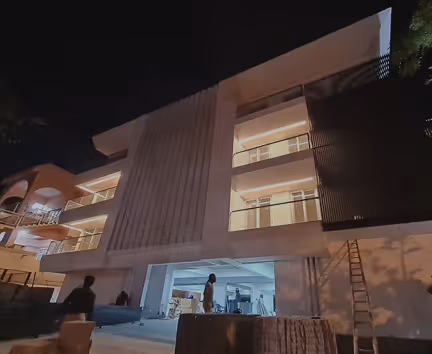Modern three-story building lit at night with people and construction materials outside.