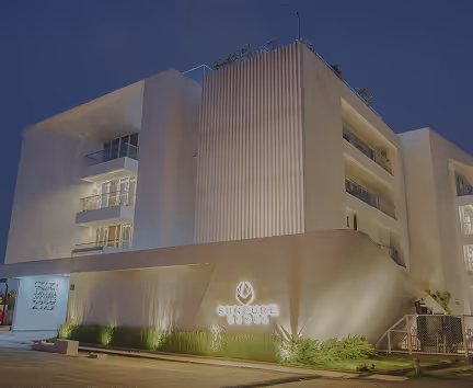 Modern white building at dusk with illuminated signage reading SURJURE 1994 and outdoor lighting.