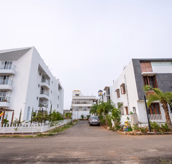 Street view of modern white residential buildings with balconies and greenery on both sides.