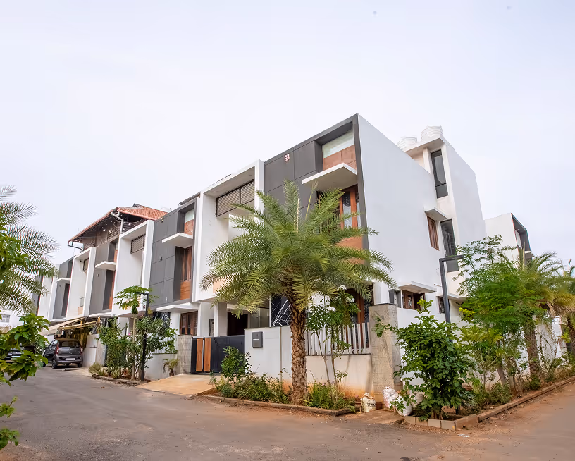 Modern white and gray multi-story residential building with palm trees and greenery around it.