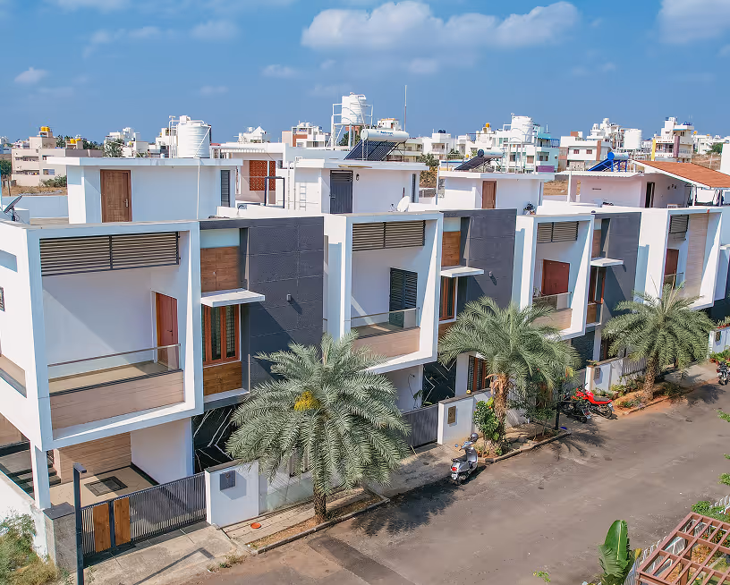 Modern white multi-story houses with palm trees lining the street on a sunny day.