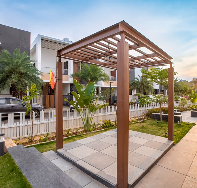 Wooden pergola on a tiled patio area with modern houses and greenery in the background.