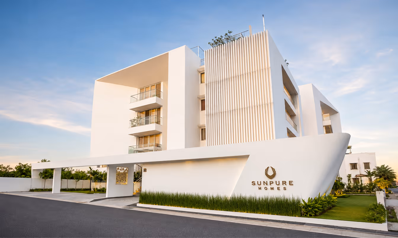 Modern white residential building entrance with Sunpure Homes logo and green landscaping in front.