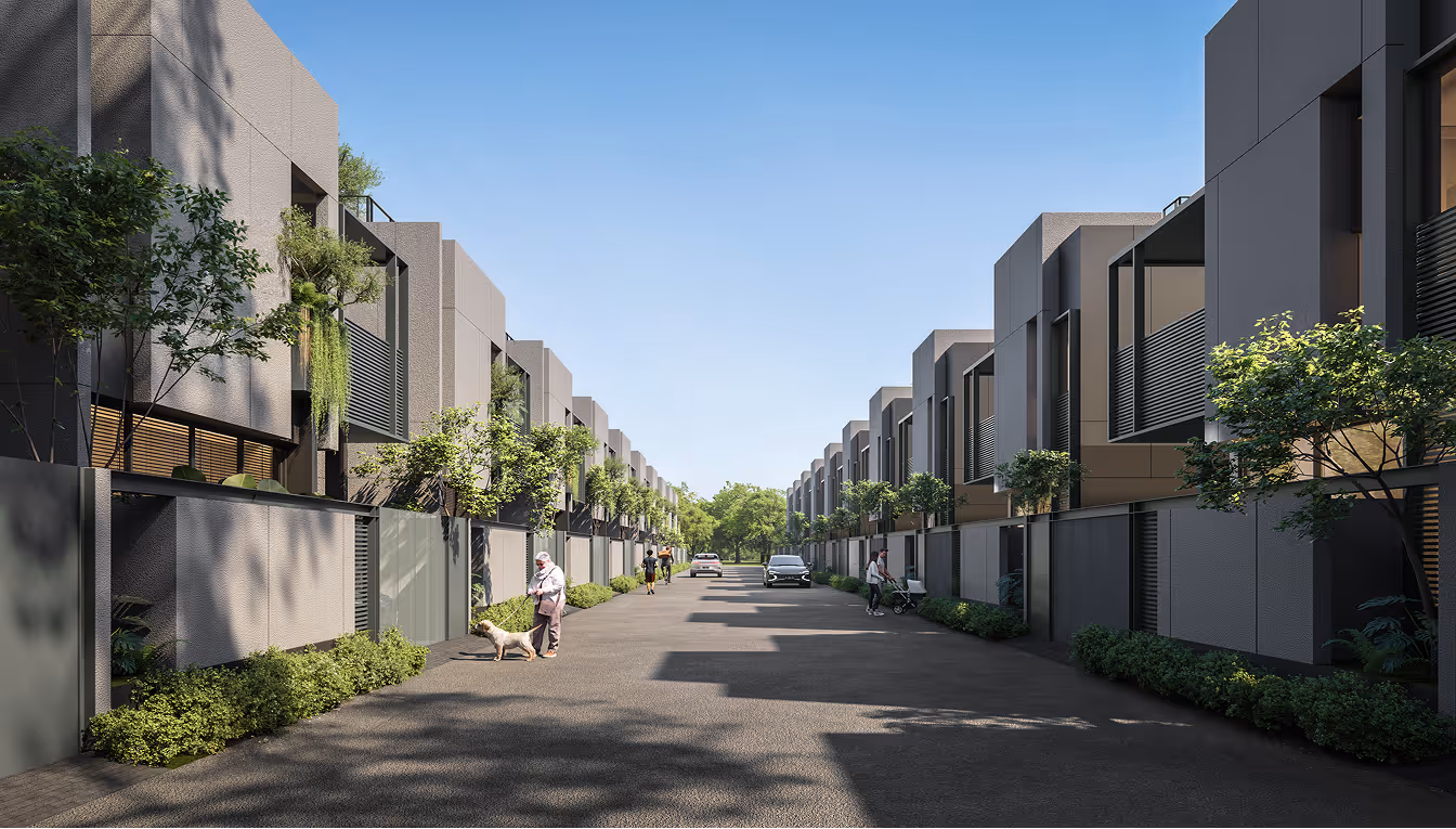 Modern townhouses with trees and shrubs along a wide street under a clear blue sky.