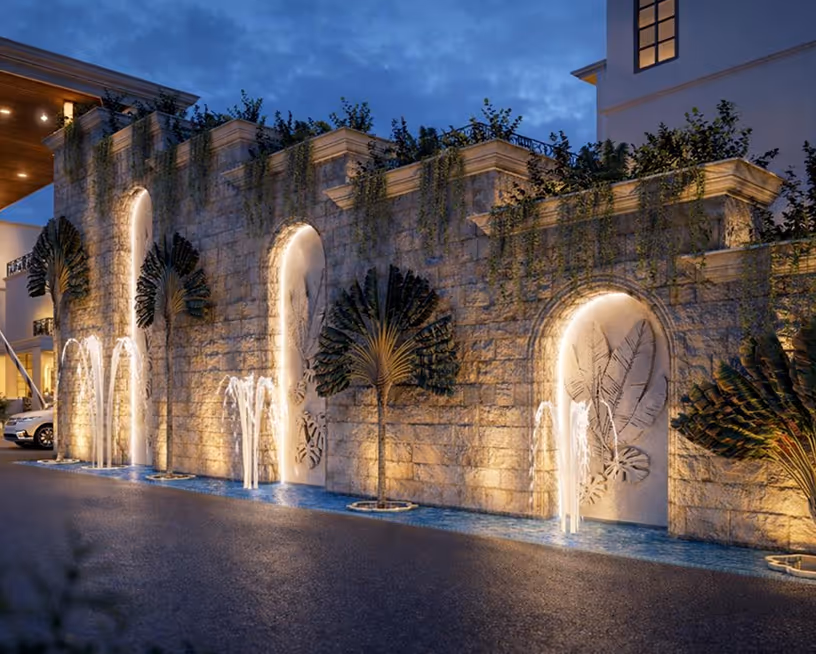 Lit stone wall with arch niches and water fountains spilling into a narrow blue pool at night.