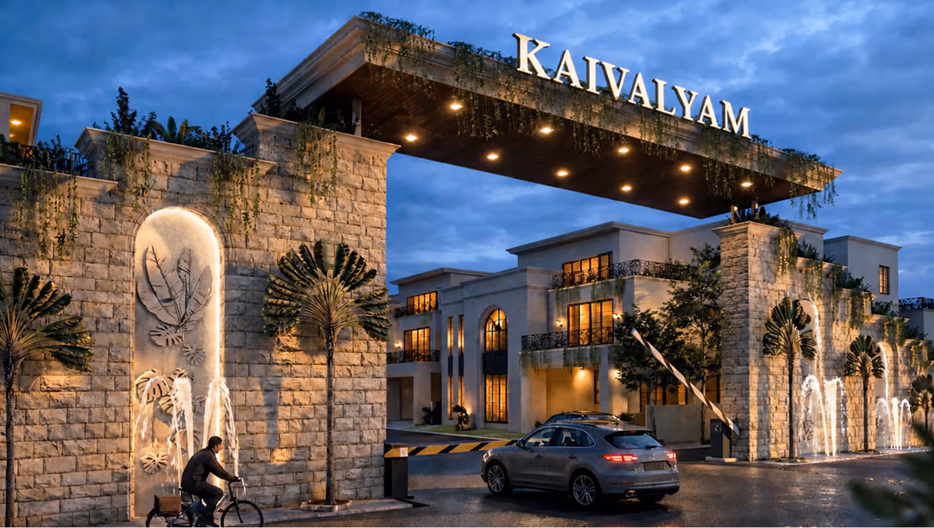 Entrance gate of Kaivalyam residential complex at dusk with a cyclist and a car passing through.