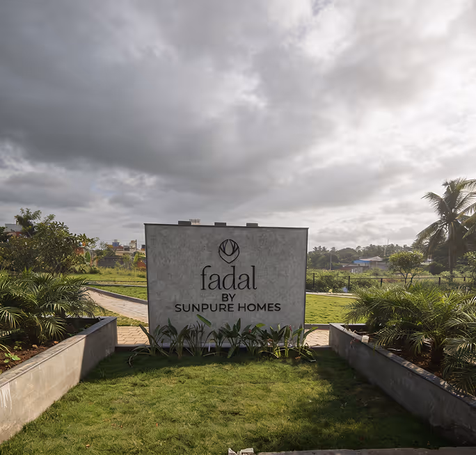 Concrete sign reading 'fadal by SUNPURE HOMES' in a landscaped area with plants and cloudy sky.