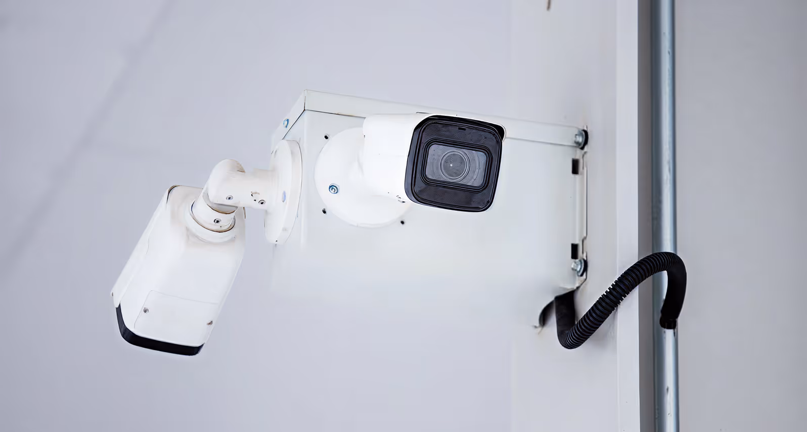 White CCTV surveillance camera mounted on a white wall with a black cable.