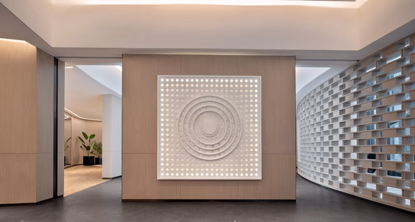 Modern hallway with light wood paneling, backlit circular wall art, and curved white lattice wall.