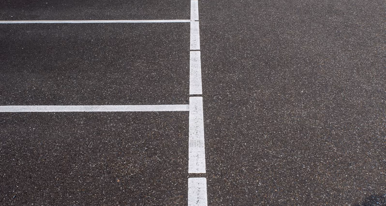Empty asphalt parking lot with white painted lines marking parking spaces.