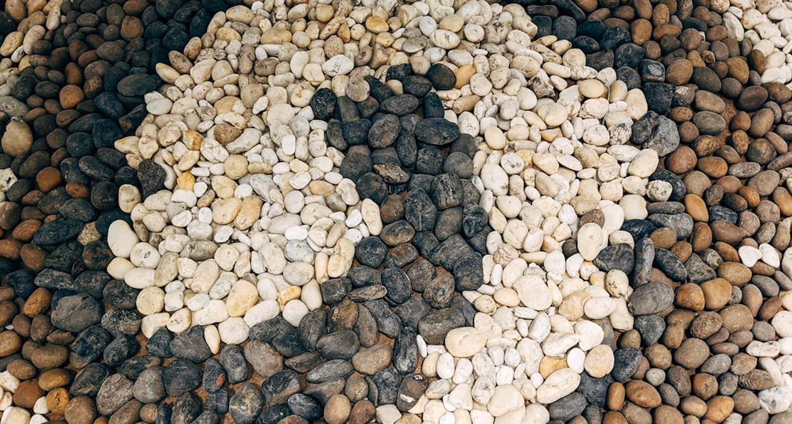 Path made of arranged smooth stones in white, black, and brown forming a pattern.