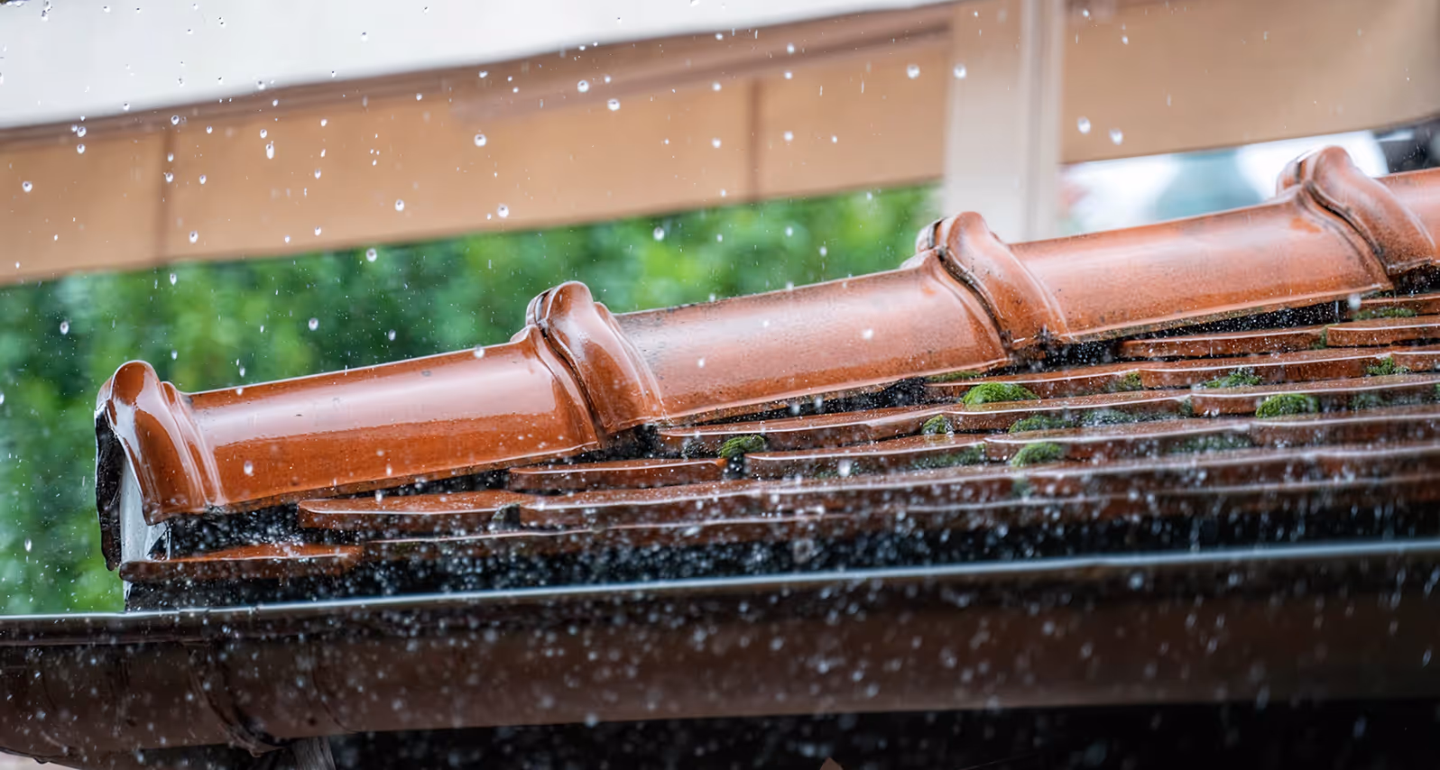 Raindrops falling on a brown tiled roof with patches of green moss.