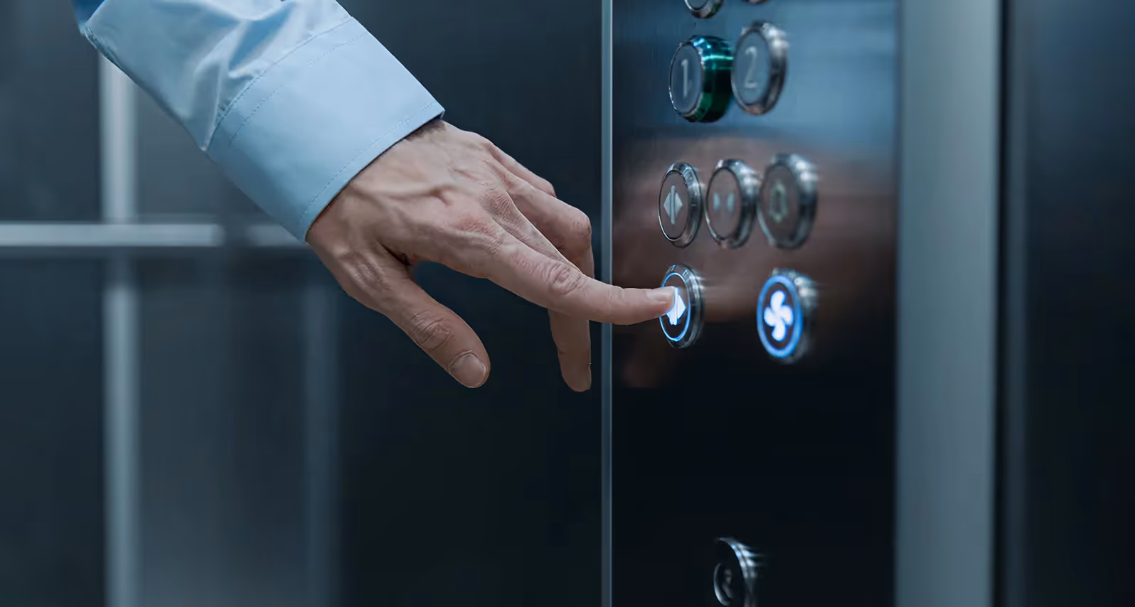 Hand pressing the elevator door close button on a modern control panel.