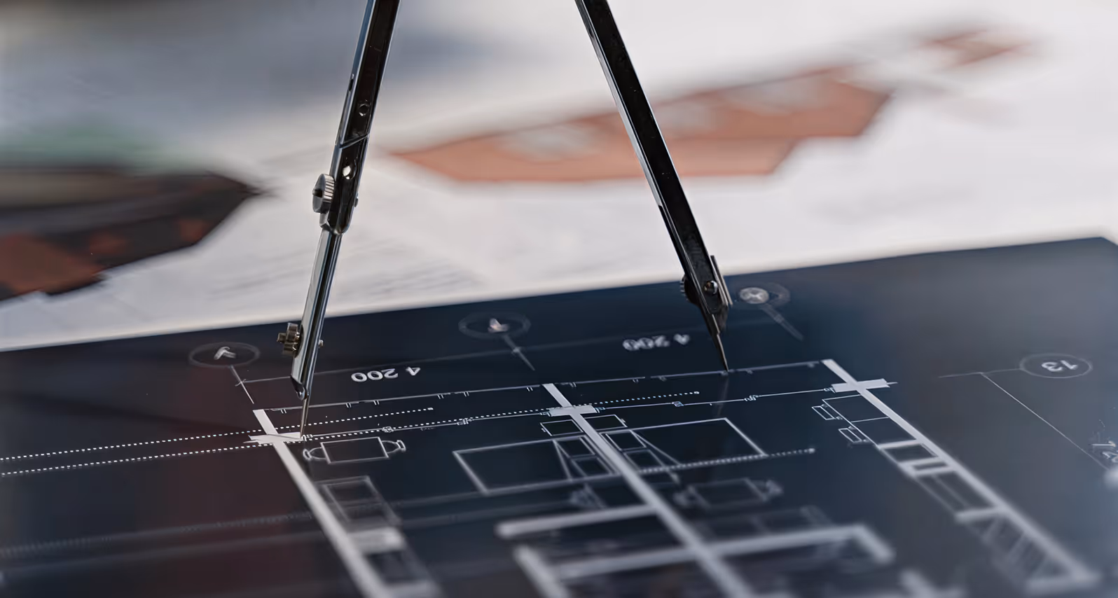 A metal compass positioned on a detailed architectural blueprint with measurements and floor plans.