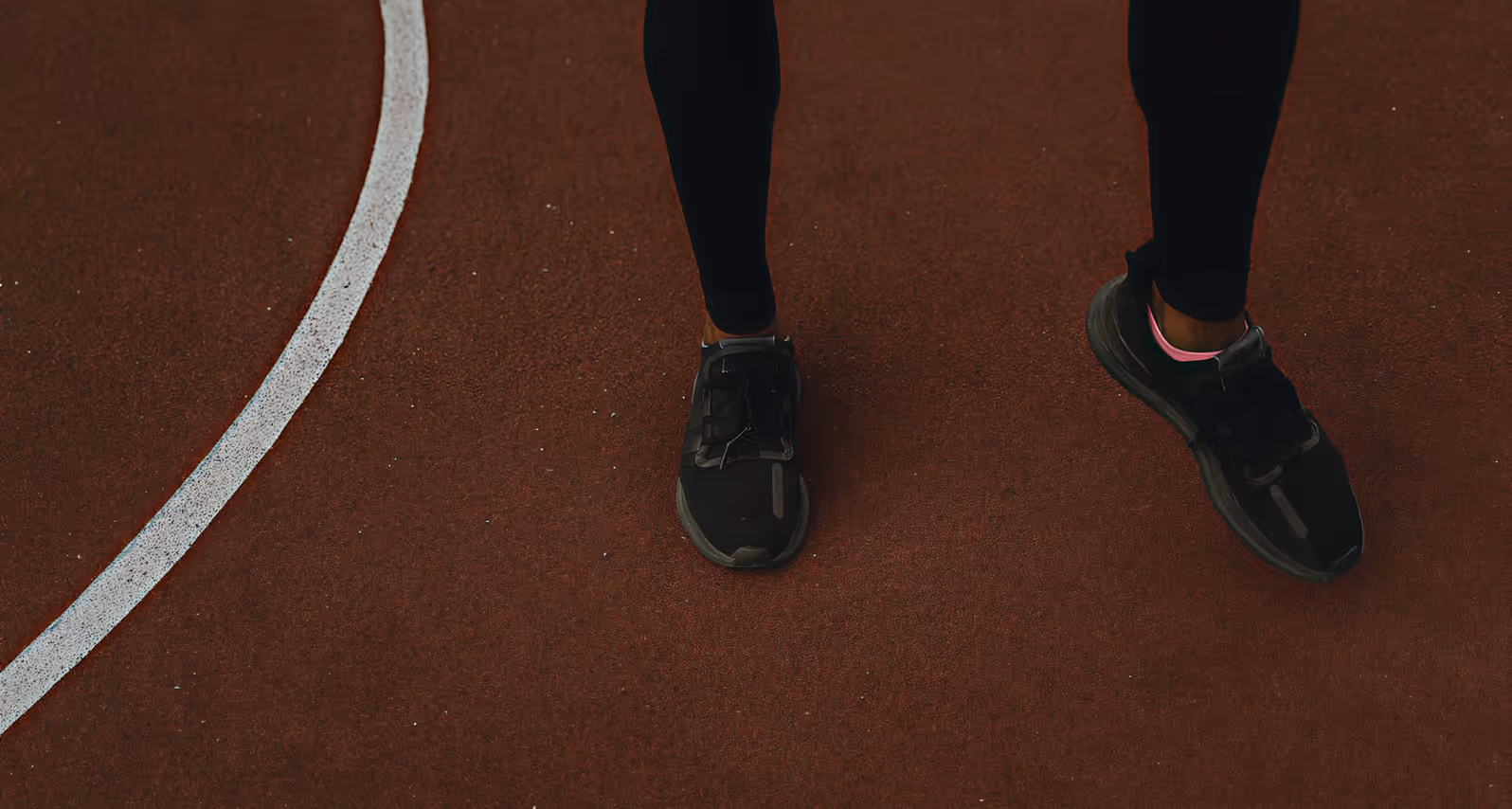 Close-up of a person wearing black sneakers and tights on a red track surface near a white line.