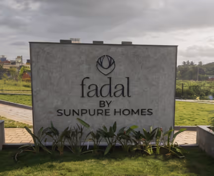 Outdoor sign with logo and text: fadal by Sunpure Homes on a concrete panel with grass and plants.