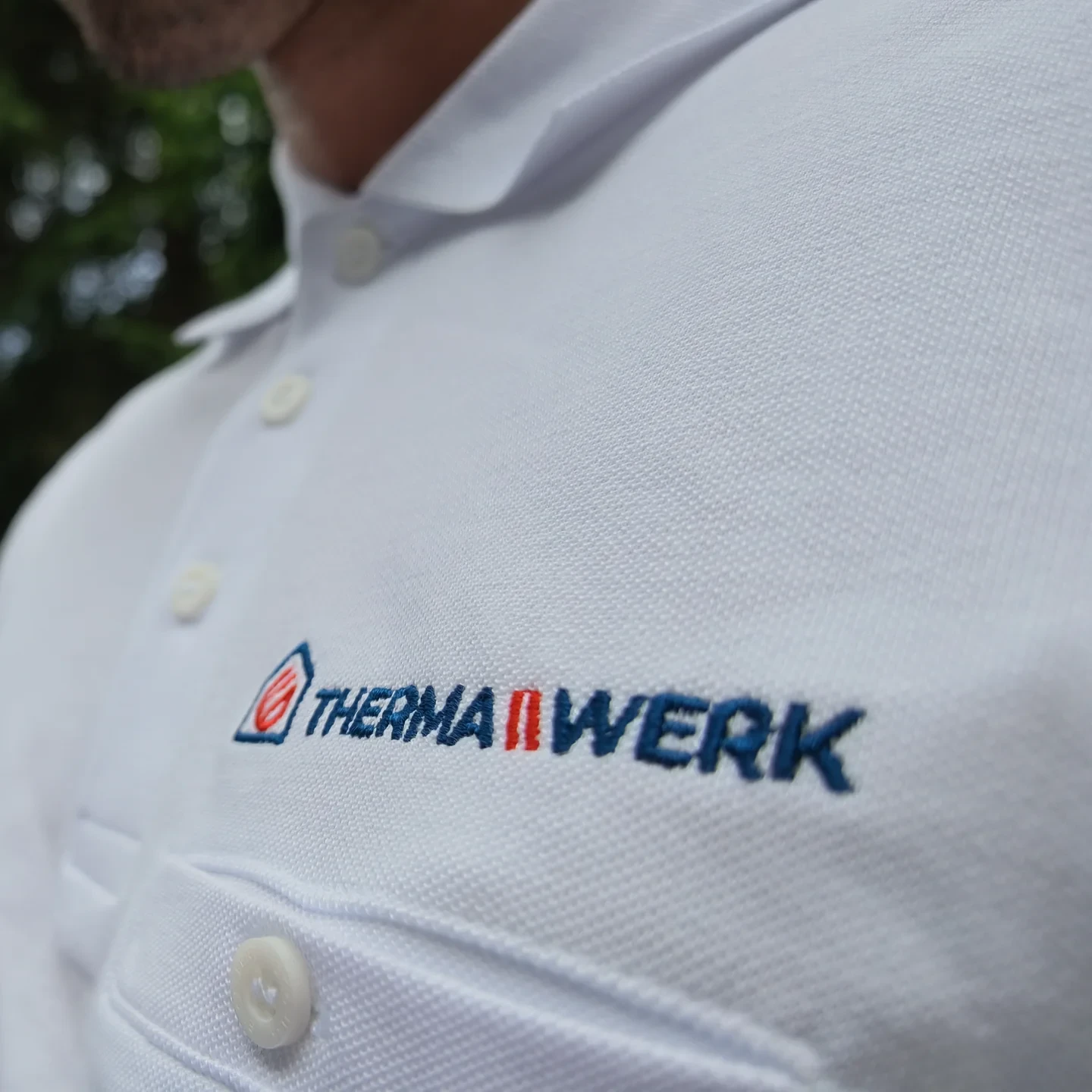 Gesticktes ThermaWerk-Logo auf dem weißen Polohemd der Firmenkleidung