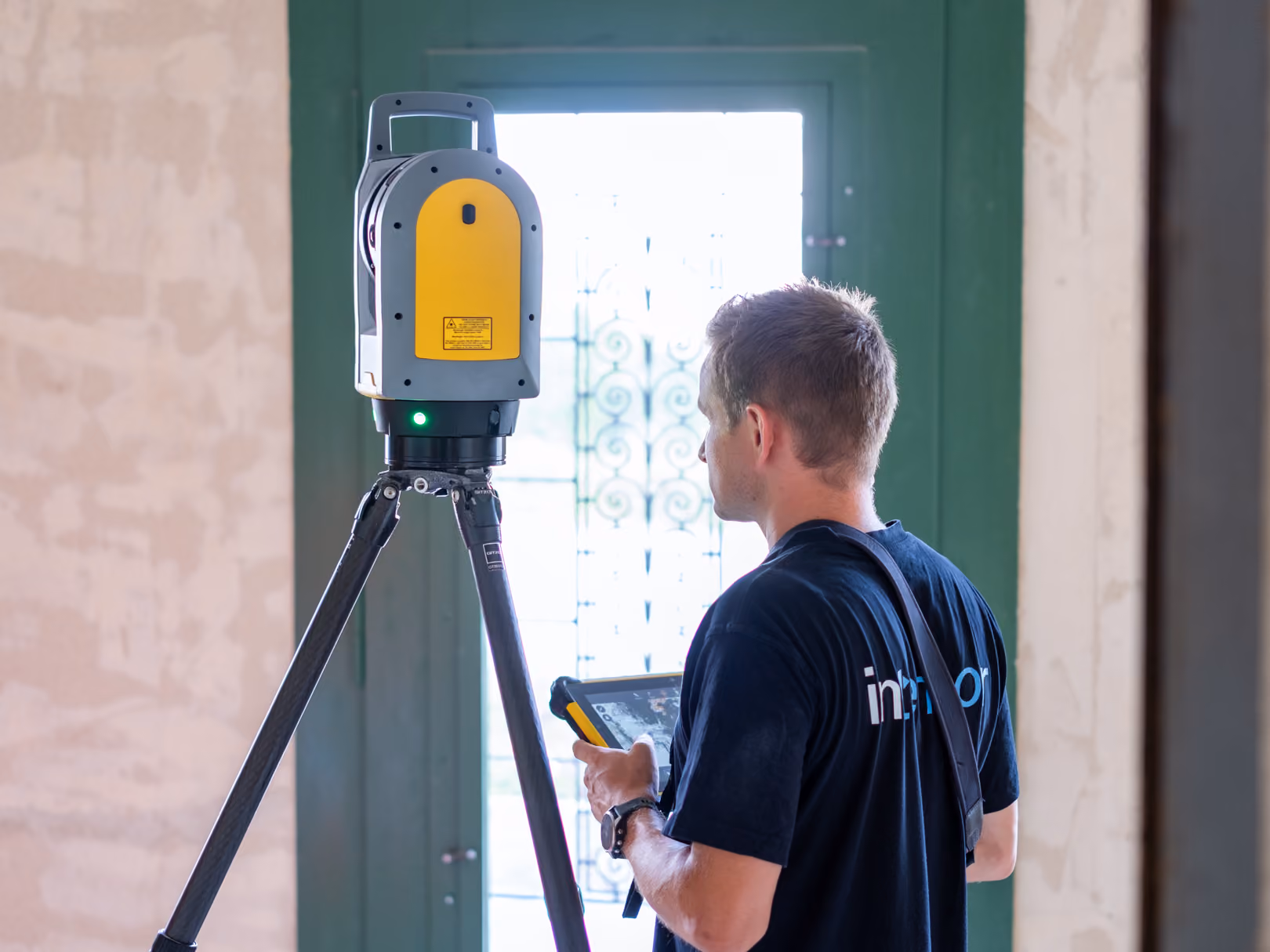 Techniker bedient ein Vermessungsgerät auf Stativ in einem Raum mit grünem Fenster.