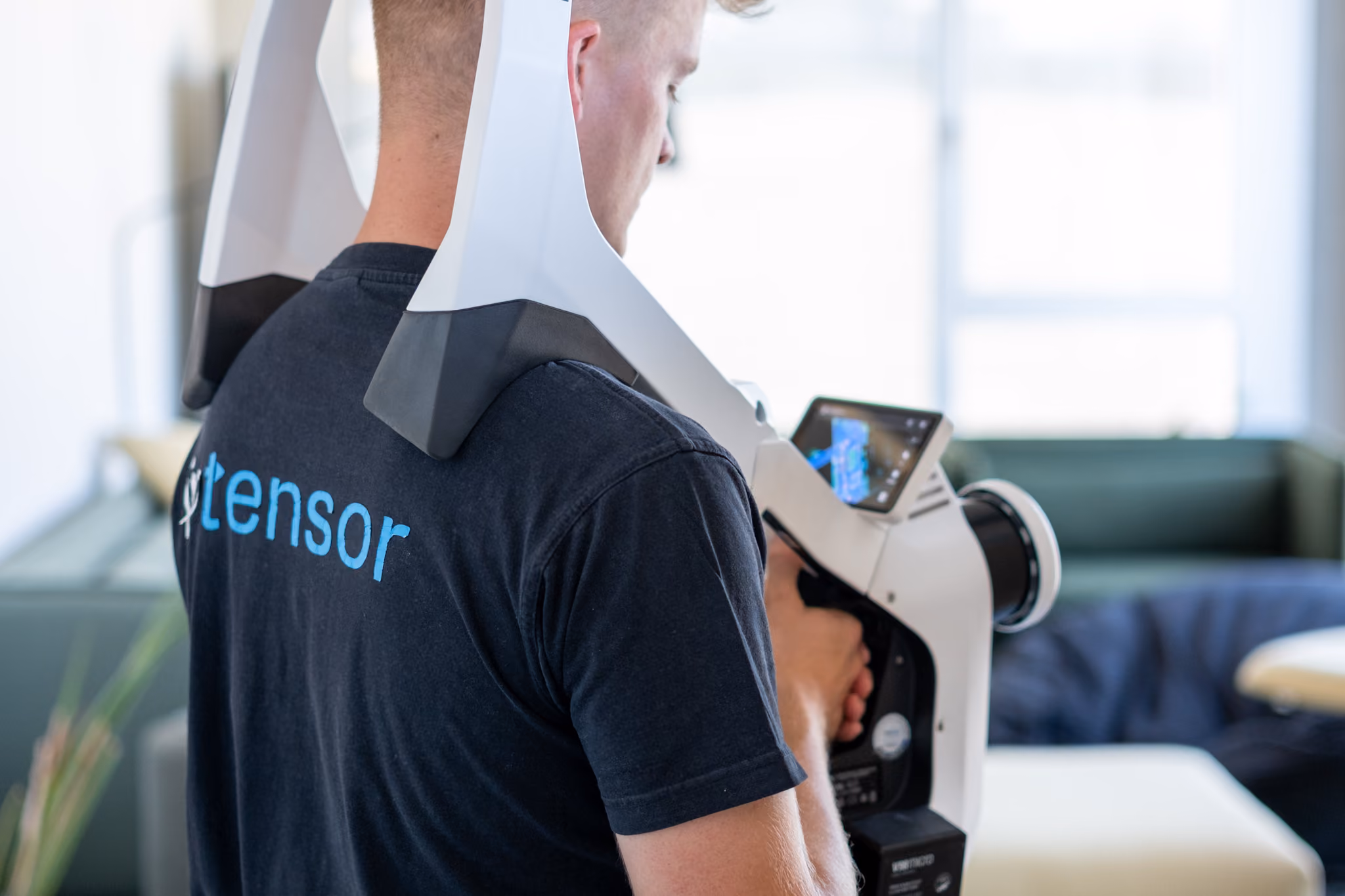 Person holding a white handheld 3D scanner with a screen in a bright room.