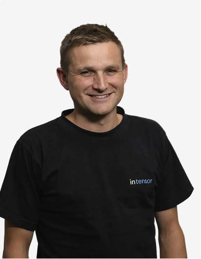 Lächelnder Mann mit kurzem Haar trägt ein schwarzes T-Shirt mit dem Aufdruck 'intensor'.