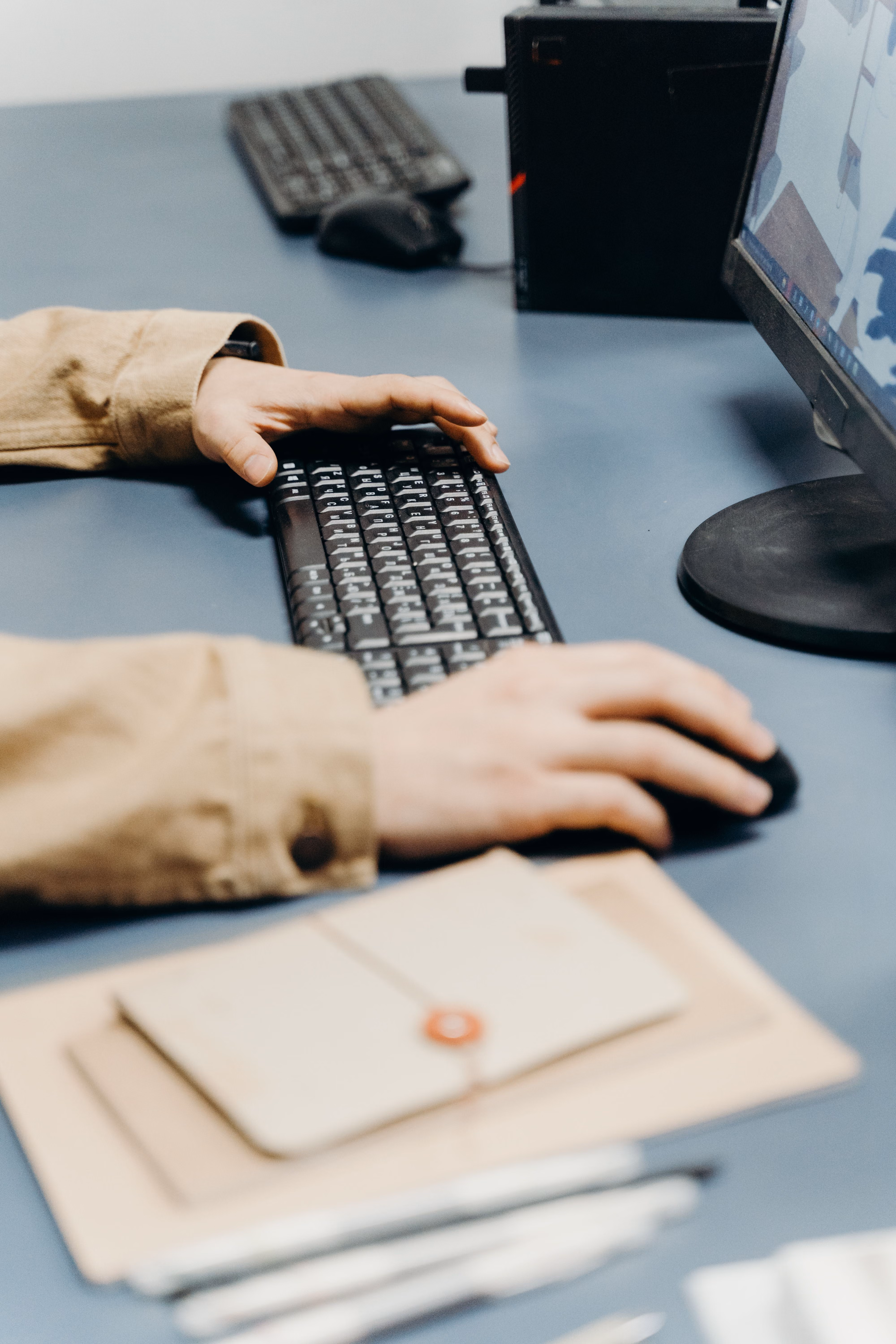 Person working at desk using keyboard and mouse with monitor and papers nearby.