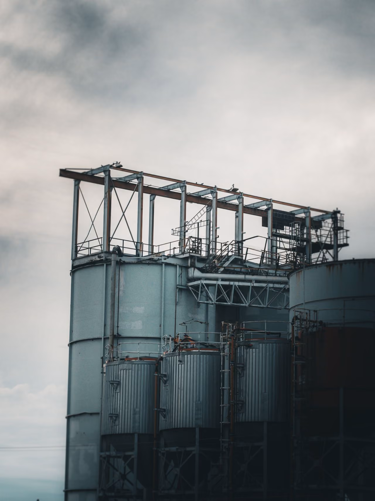 Industrieanlage mit großen Metalltanks und einem Gerüst unter einem bewölkten Himmel.