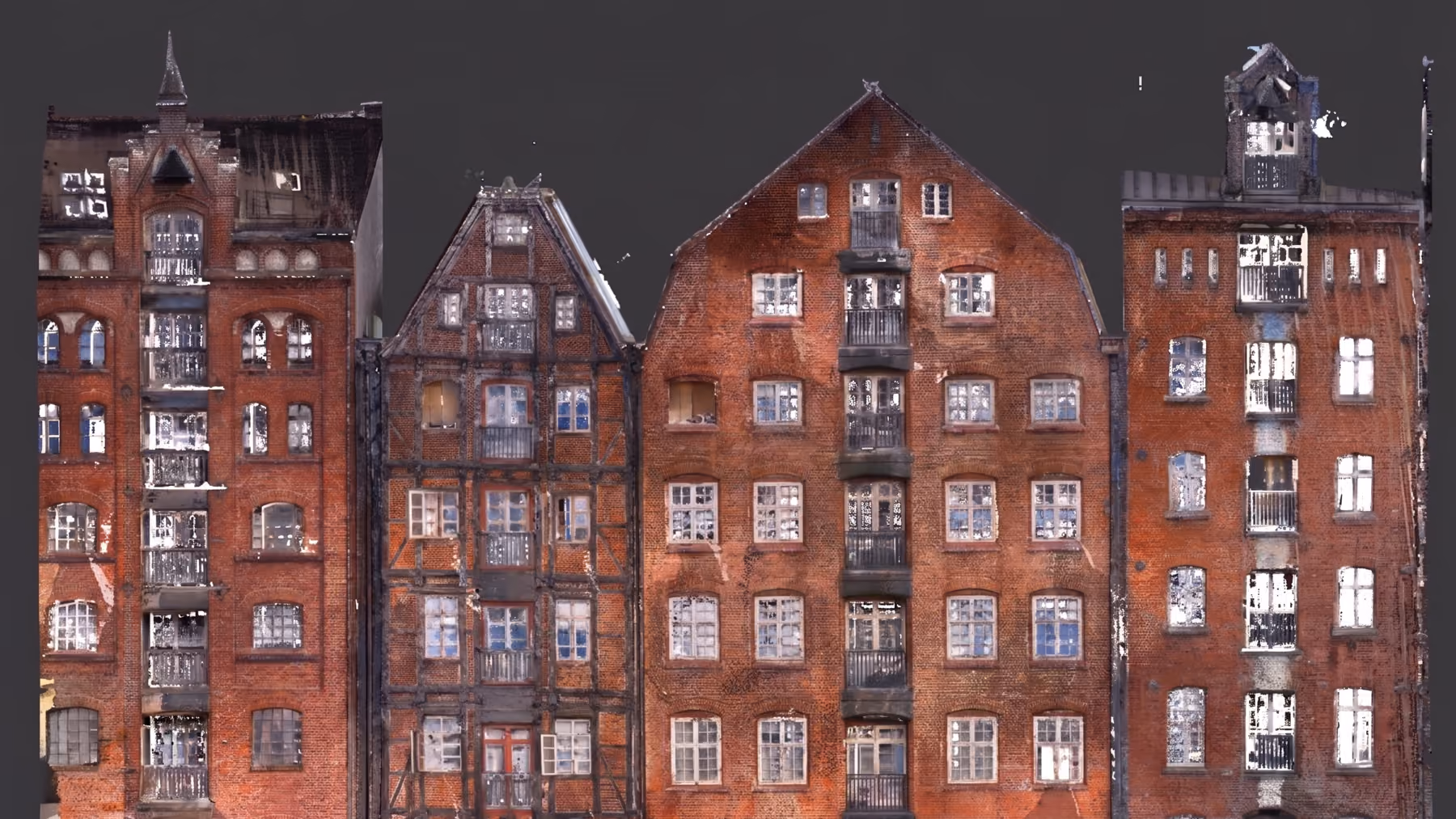 Fassade von vier historischen Speichergebäuden aus rotem Backstein mit zahlreichen weißen Fenstern und schwarzen Balkonen vor dunklem Hintergrund.