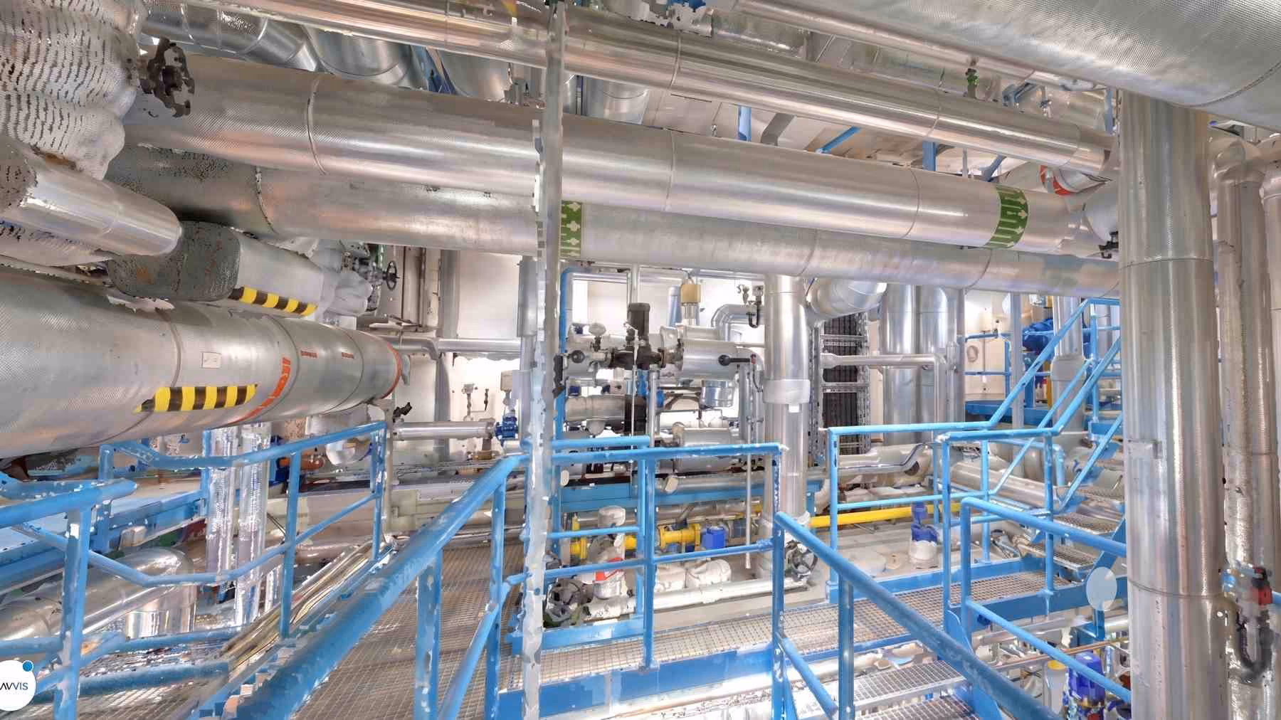 Industrielle Anlage mit zahlreichen silbernen Rohren, Ventilen und blauen Geländern in einem technischen Raum.