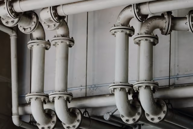 Weiße Metallrohre mit Flanschverbindungen auf einer grauen Wand montiert.