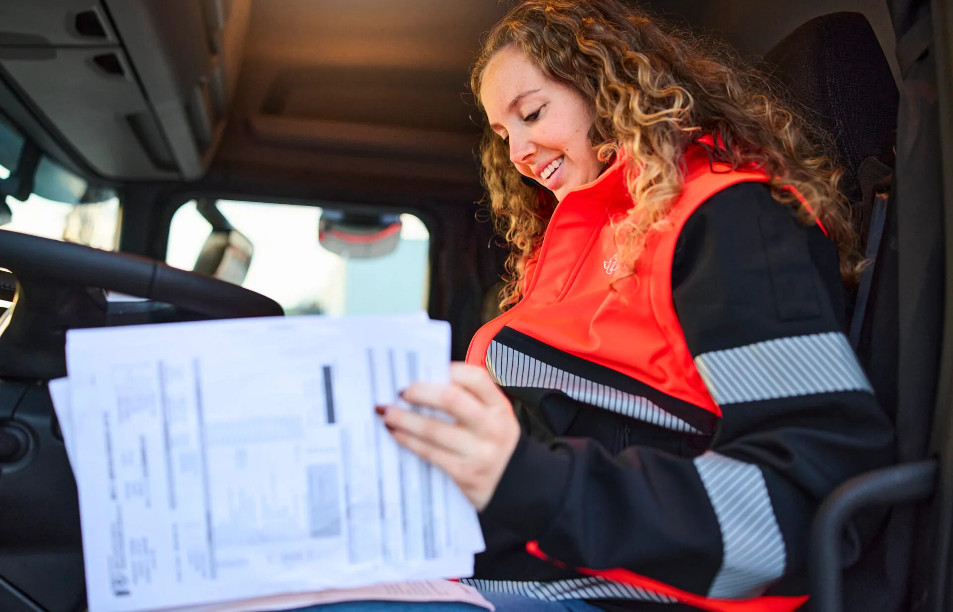 Vrouwelijke chauffeur bekijkt lachend de vrachtbrieven in de cabine van een vrachtwagen