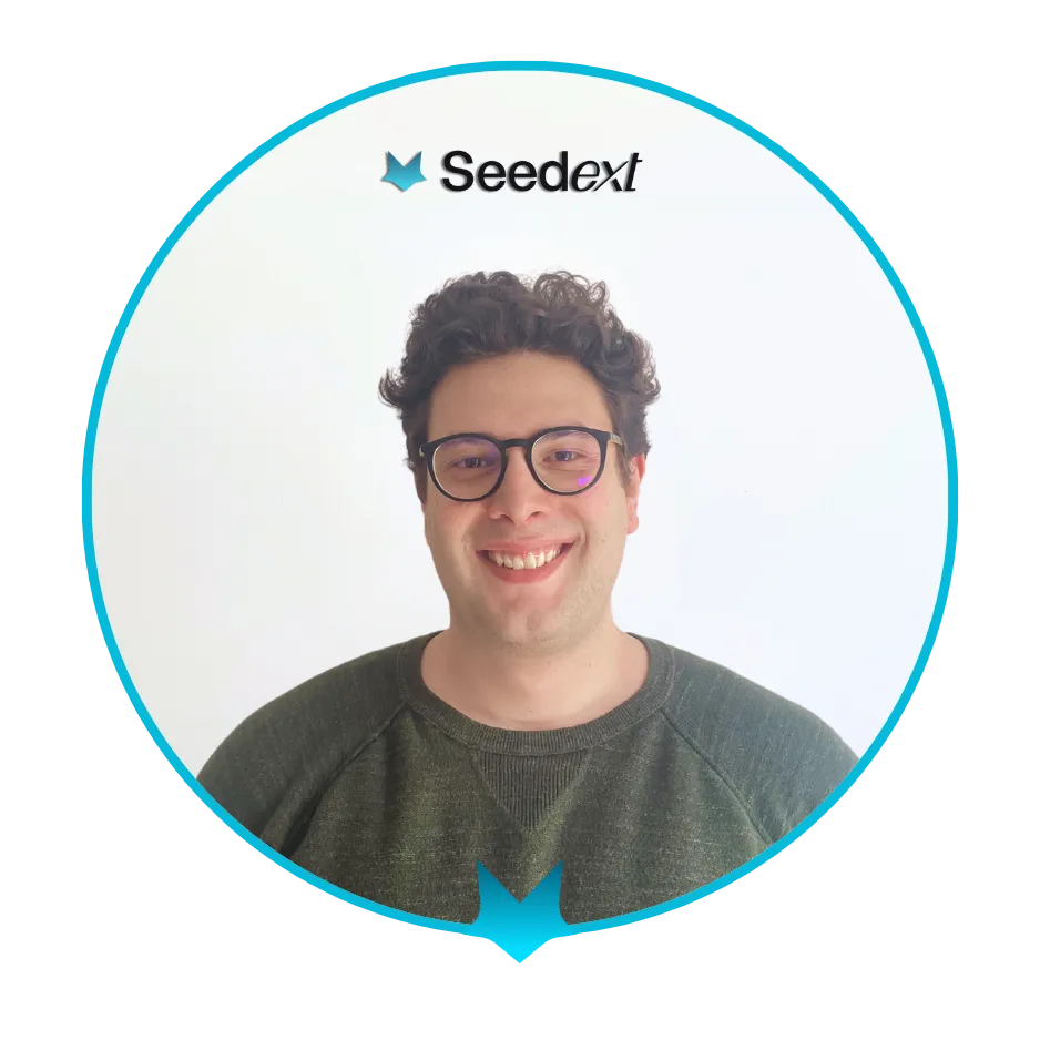 Jeune homme souriant avec des lunettes et un pull vert, encadré par un cercle bleu avec le logo Seedext en haut.
