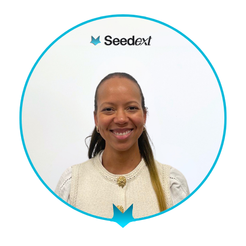 Portrait souriant d'une femme portant un gilet beige avec un bouton doré, fond blanc avec le logo Seedext au-dessus.