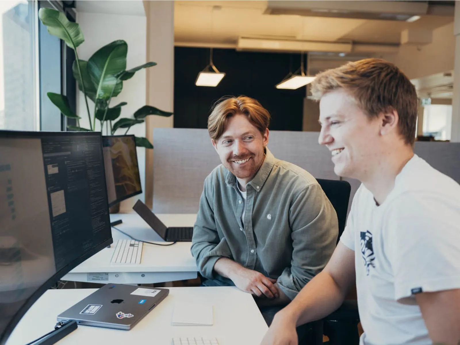 Two colleagues working together at a desk with monitors.