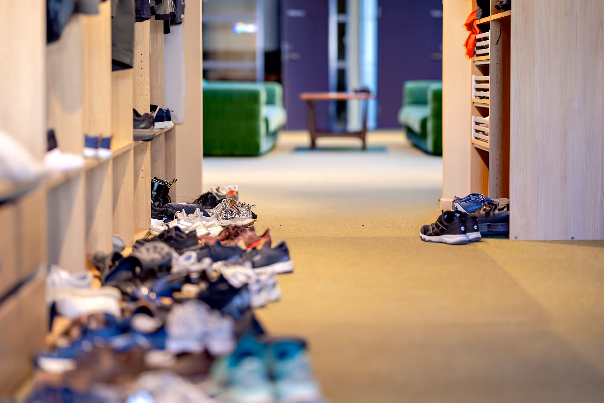 Hallway with shoes scattered on the floor and green sofas and table in the background.