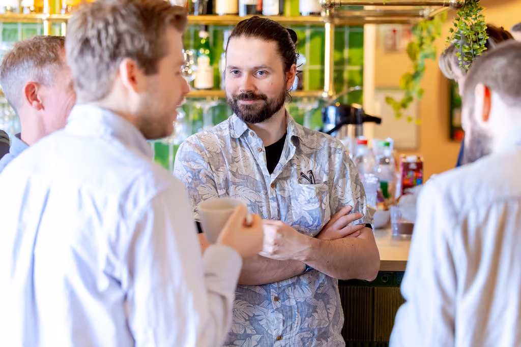 Group of men having a conversation in a casual setting, one man holding a cup and another with arms crossed.