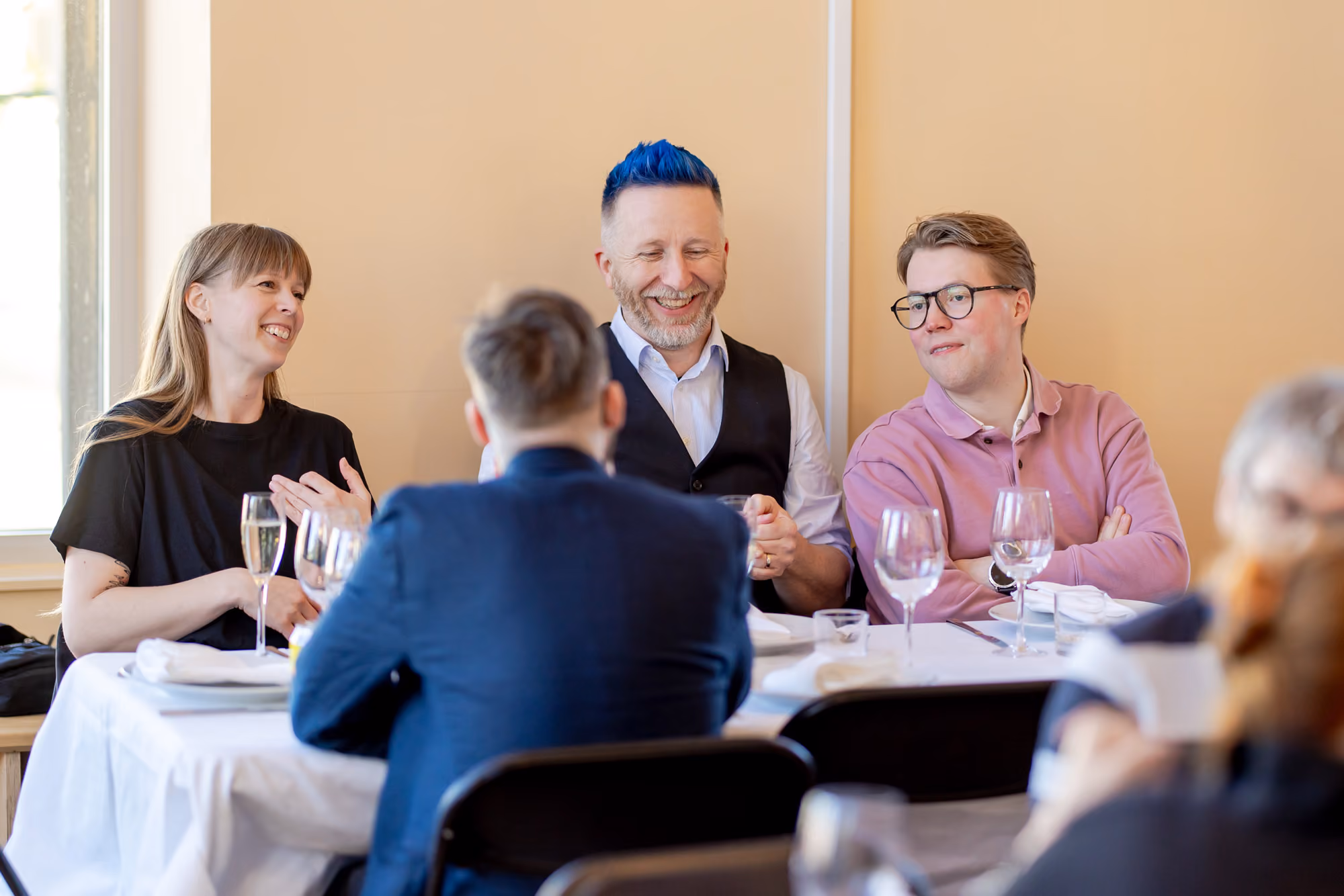 Four people seated at a table with wine glasses, talking and smiling during a social meal.