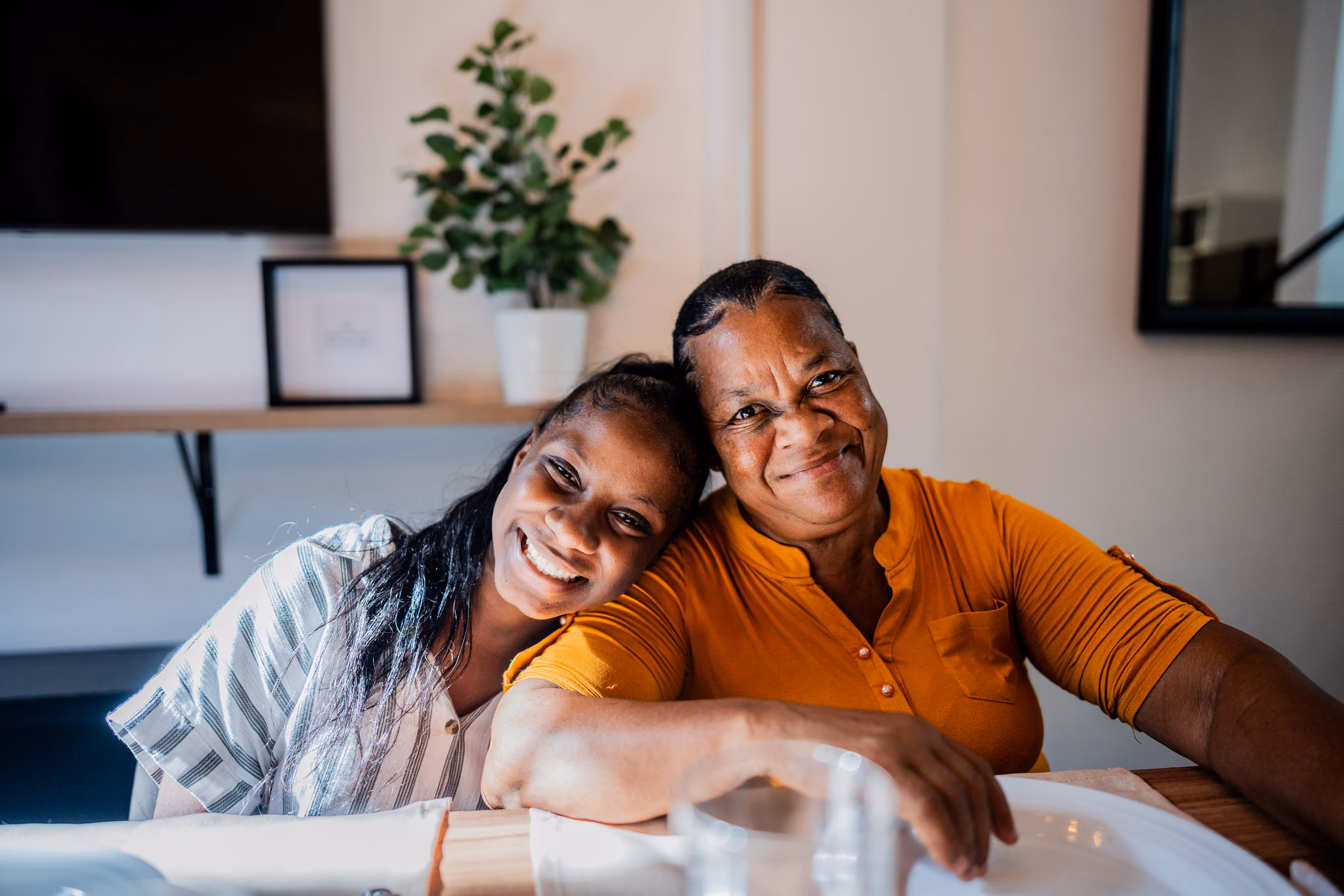 Smiling older woman and young girl sitting close together at a table in a cozy room.