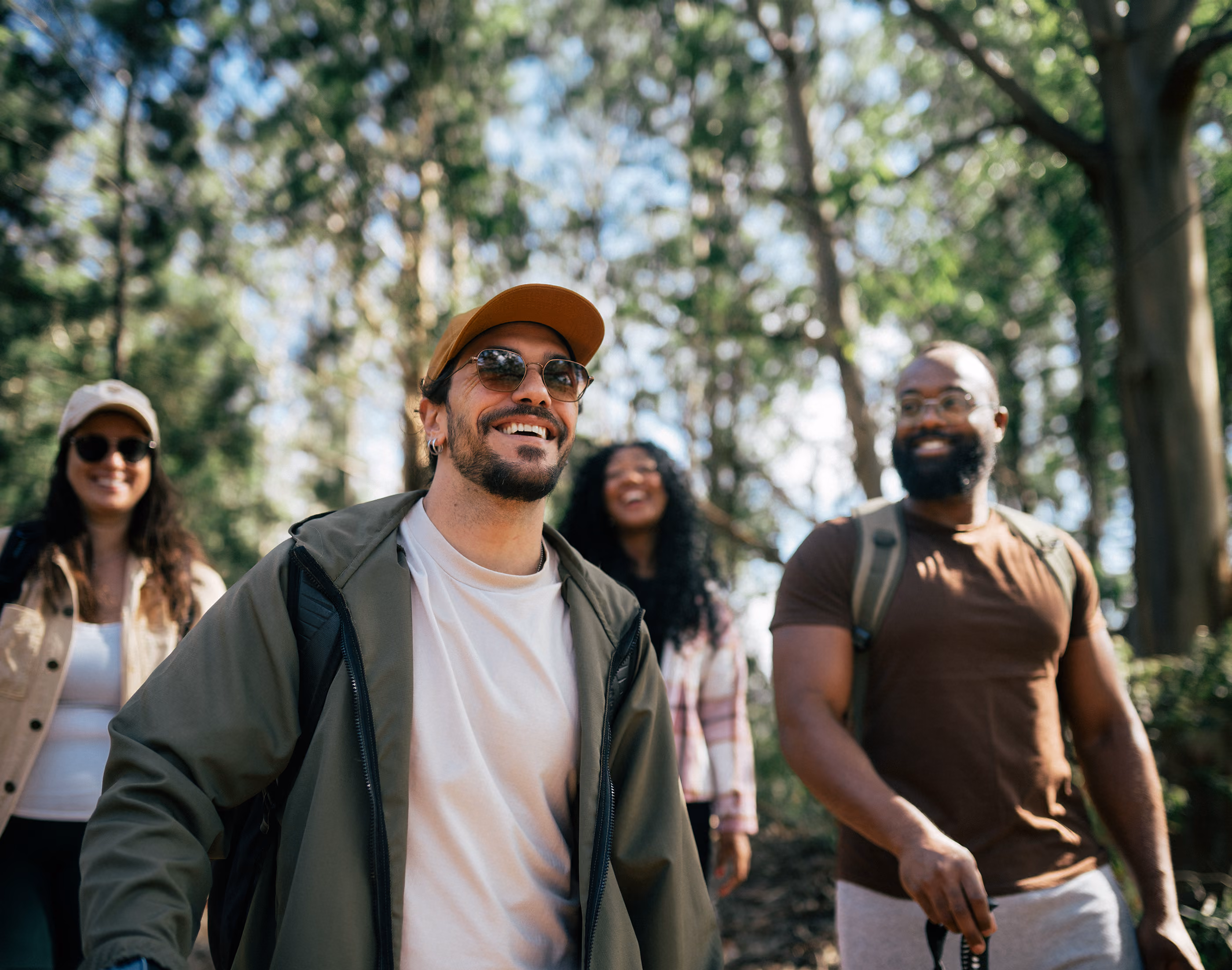 Four friends hiking in a forest, smiling and enjoying the outdoors on a sunny day.