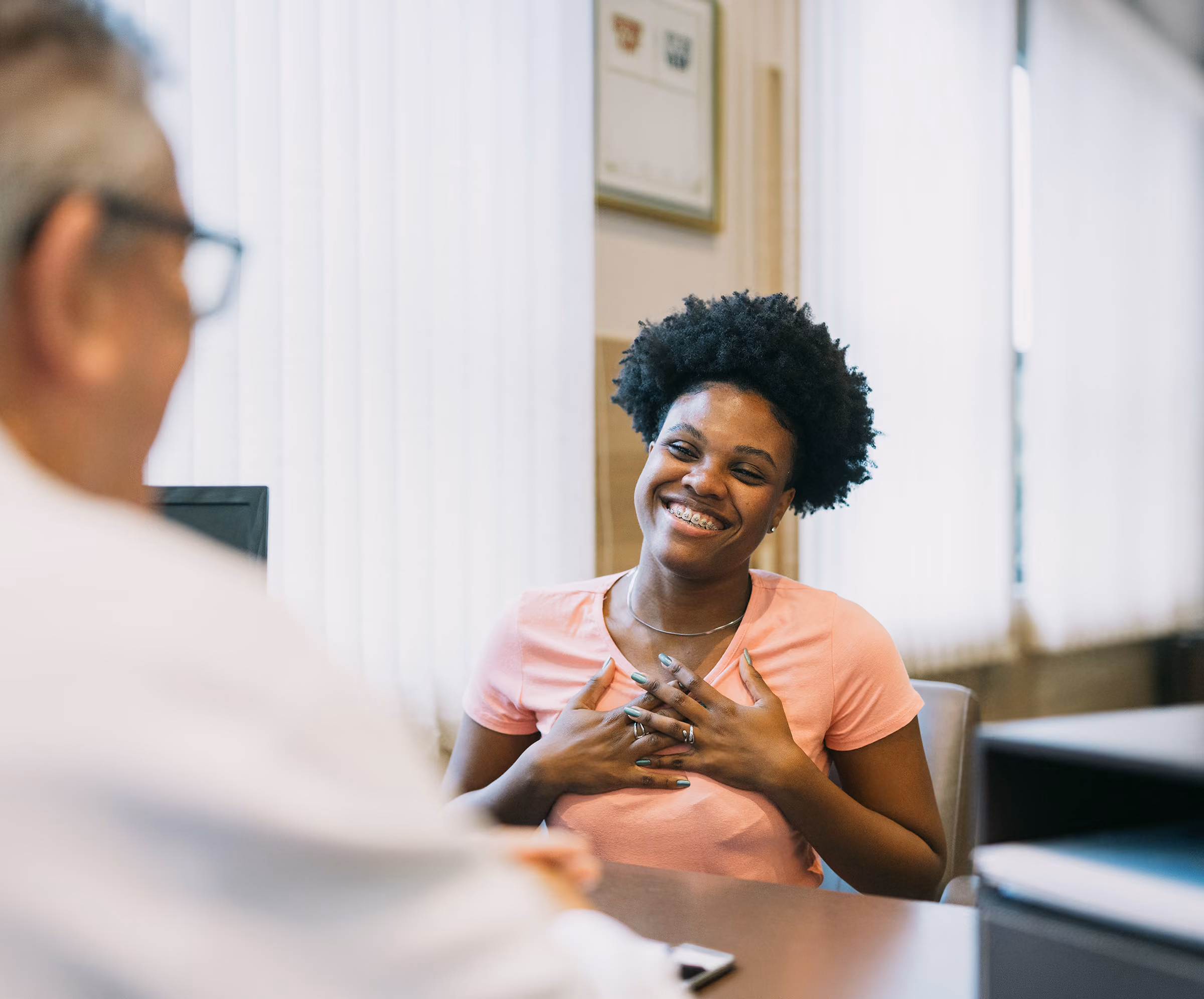 Grateful female patient gesturing happily while talking to doctor in office.