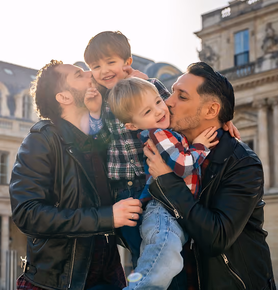 Deux hommes en vestes en cuir embrassant joyeusement deux jeunes garçons à l'extérieur.